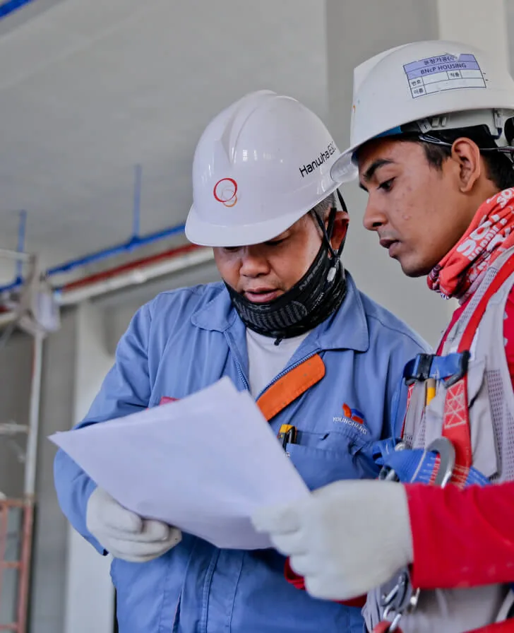 Two waterproofing professionals in hard hats reviewing plans on site